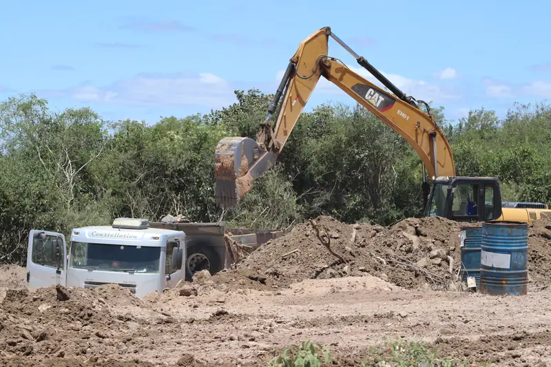 Escavadeira e caminhão em obra de abertura de vala, com acompanhamento arqueológico