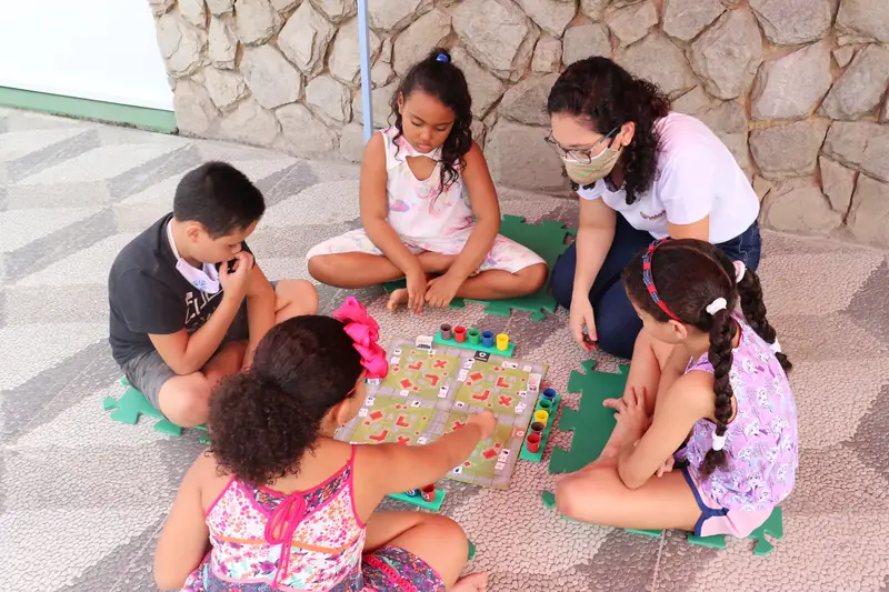 Crianças e educadoras jogando um jogo educativo no chão