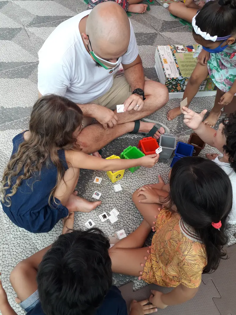 Crianças e adultos reunidos em volta de um jogo educativo