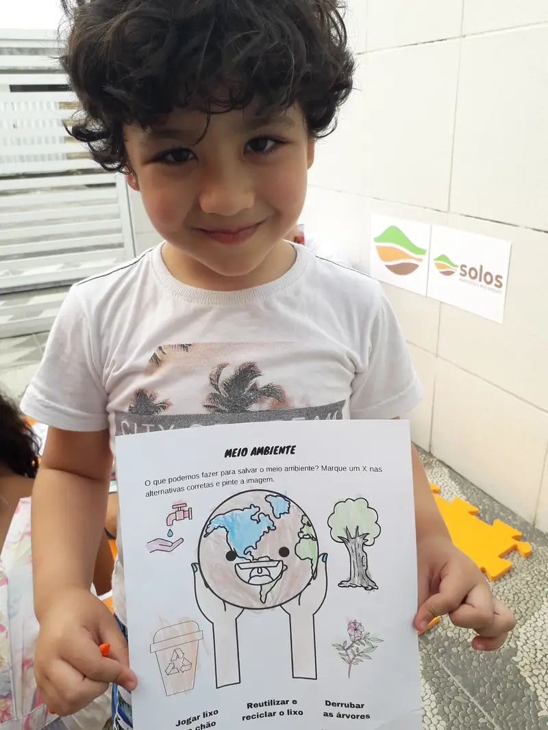 Criança sorrindo e mostrando um desenho feito na atividade