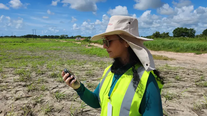 Pesquisadora de colete refletivo e chapéu usando um aparelho de GPS em campo
