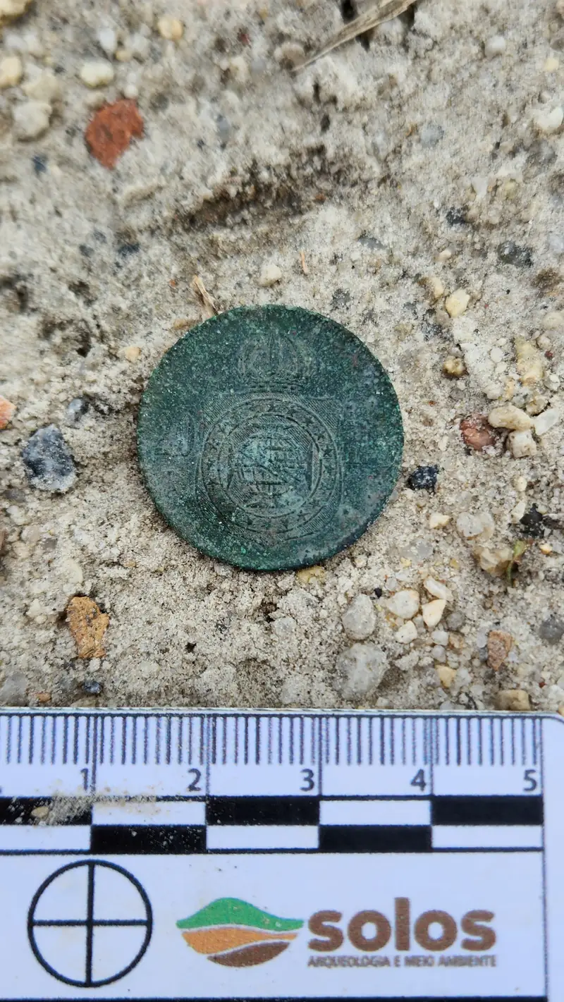 Objeto metálico circular encontrado no solo, ao lado da escala da Solos