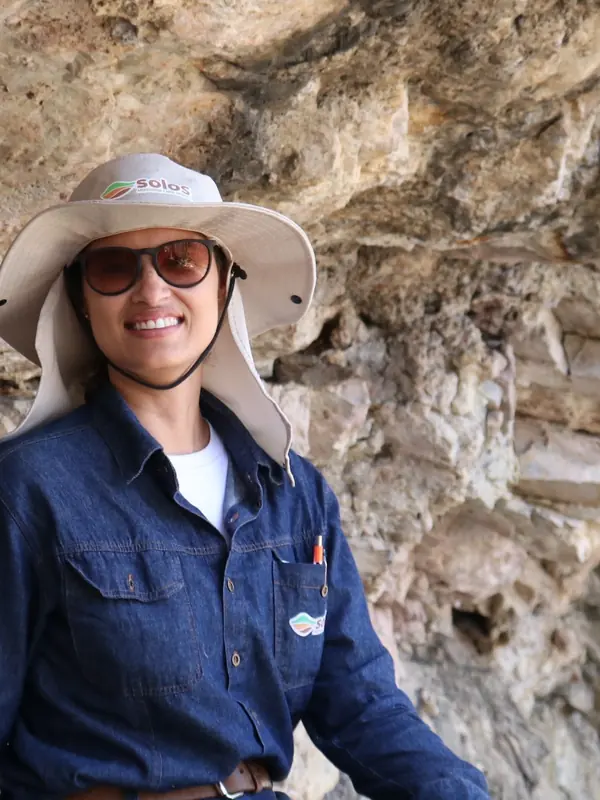 Rúbia Nogueira sorrindo em um abrigo rochoso, de chapéu e óculos escuros